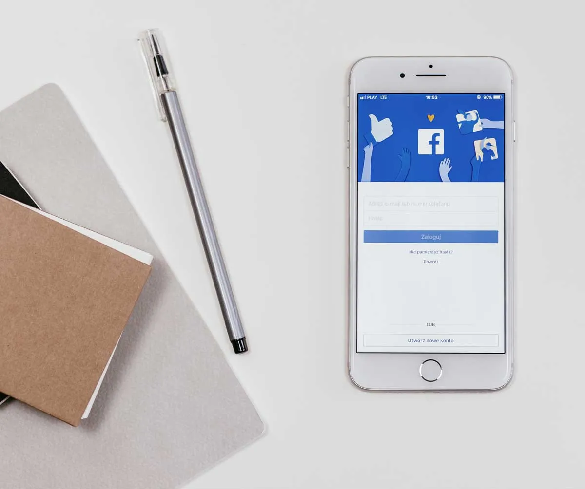 Telefon afișând o pagină de Facebook, lângă un caiet